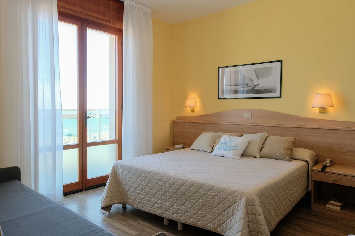 A hotel room with a large bed, two bedside tables, a nightstand, a window with curtains, and a framed picture on the wall.