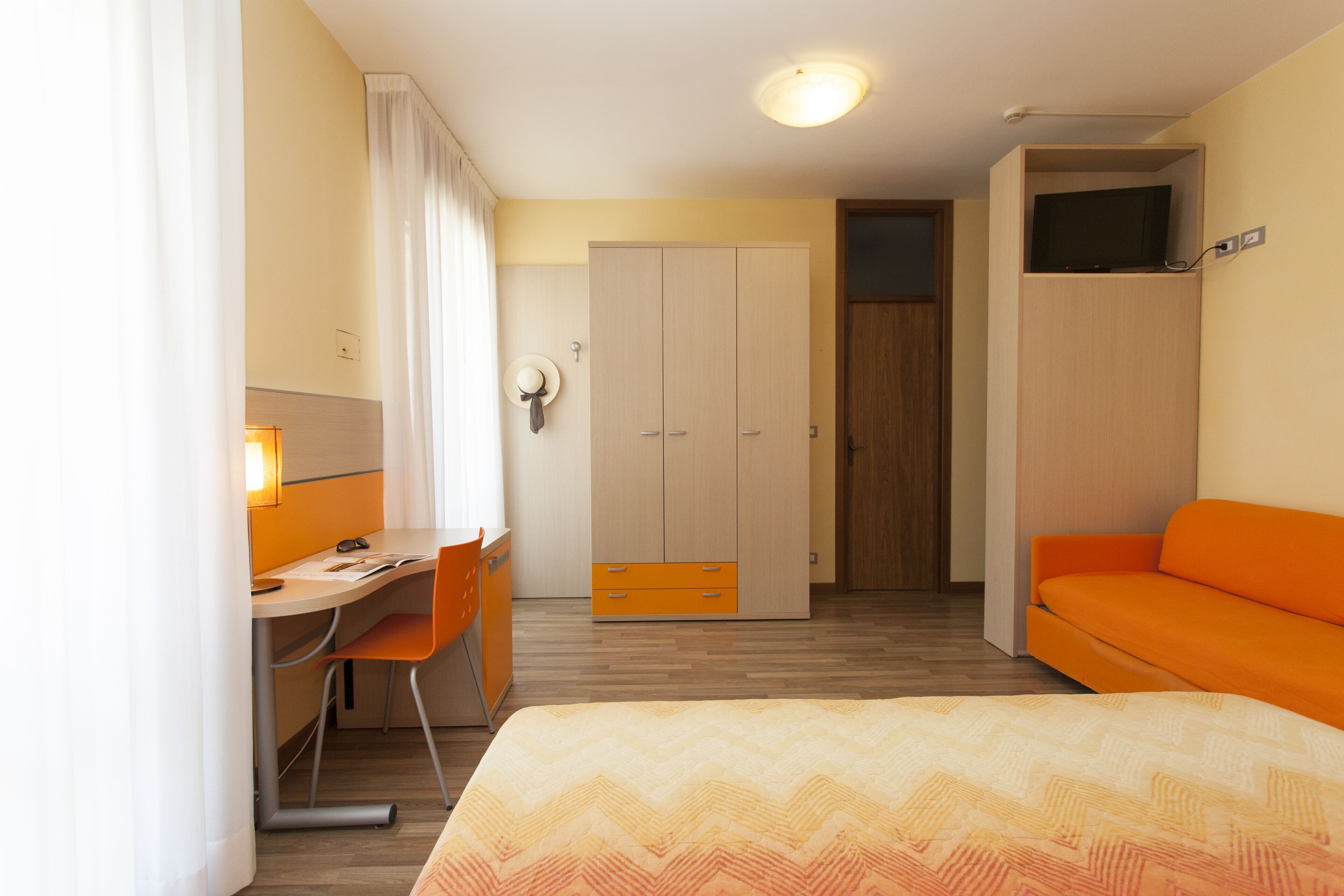A hotel room with a bed, a desk with a chair, a wardrobe, and a television.