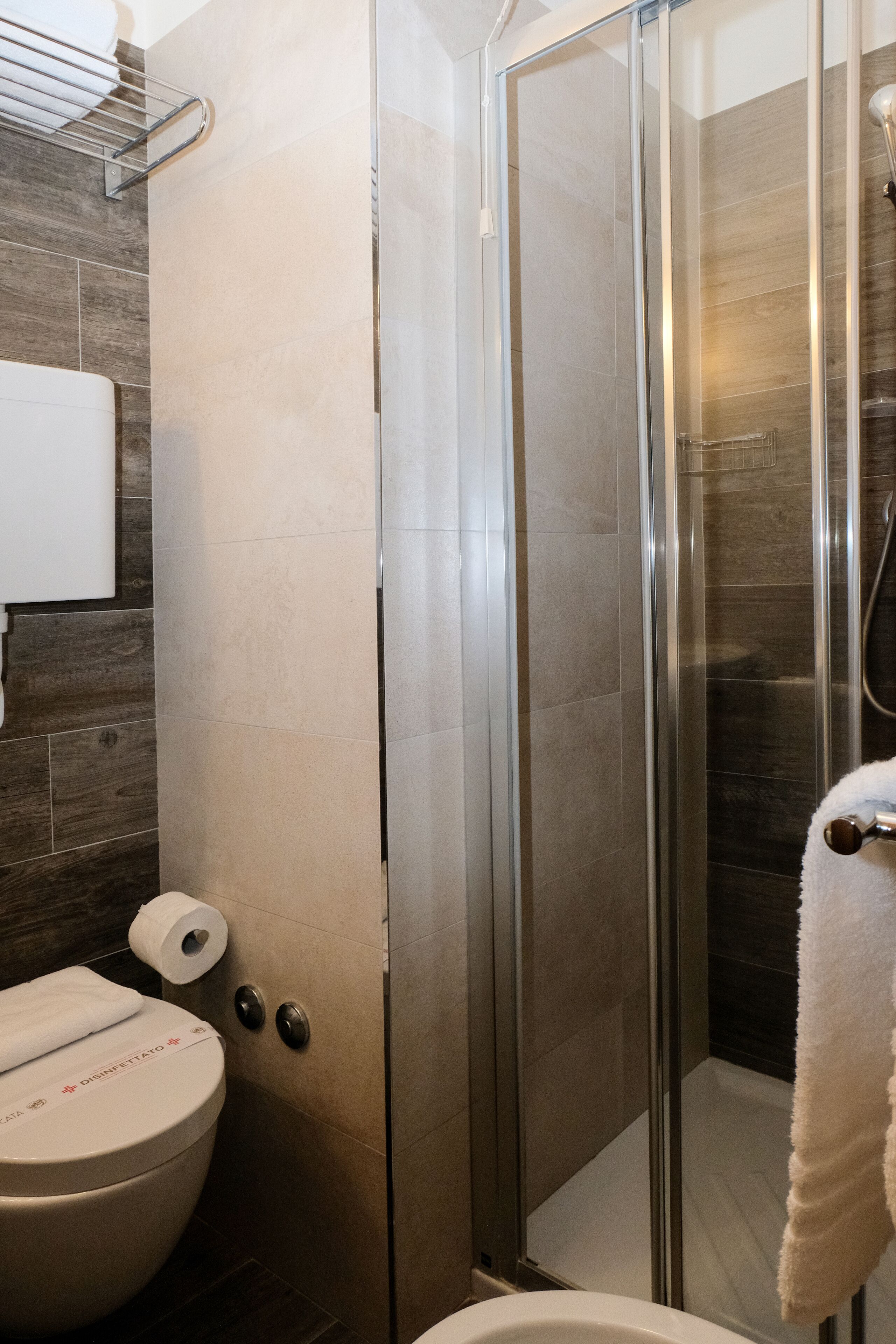 A modern bathroom with a glass-enclosed shower, a toilet with a paper towel dispenser, and a towel rack.