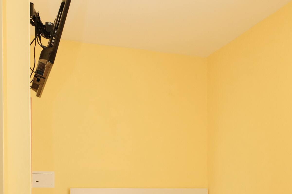 A small, yellow-walled bedroom with a single bed, a bedside table with two potted plants, and a wall-mounted lamp.