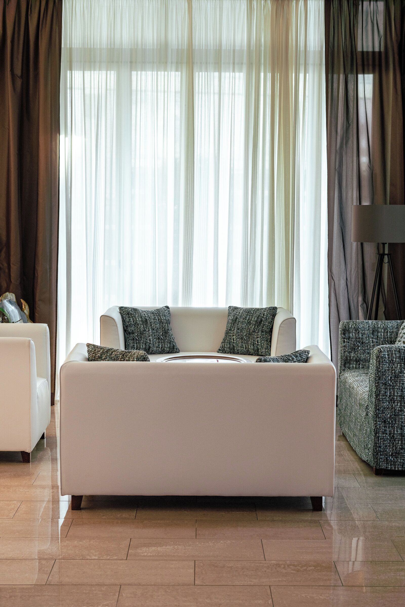 A modern living room with a white sofa, two patterned throw pillows, and a patterned armchair.