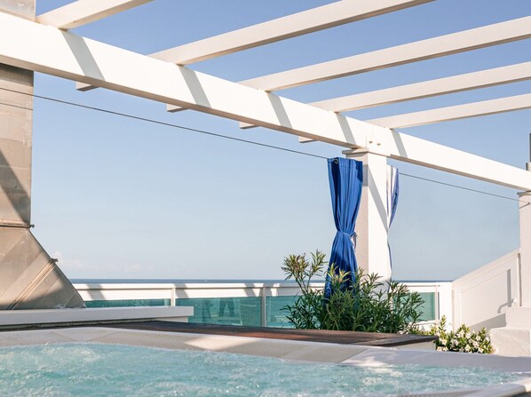 Ein Poolbereich auf dem Dach mit freiem Blick auf den Ozean, einem blauen Vorhang und einigen Grünpflanzen.