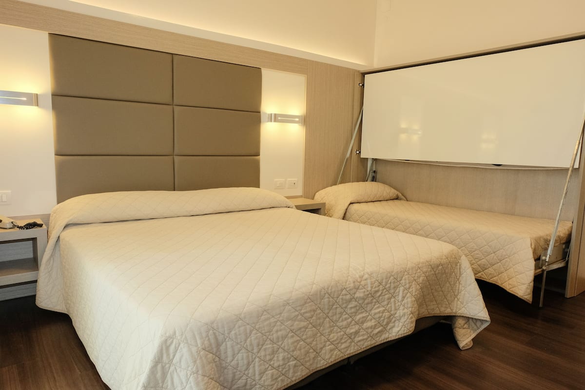 Ein Hotelzimmer mit zwei Betten, einem großen, gepolsterten Kopfteil, einem Nachttisch mit Lampe sowie einer Tafel an der Wand.