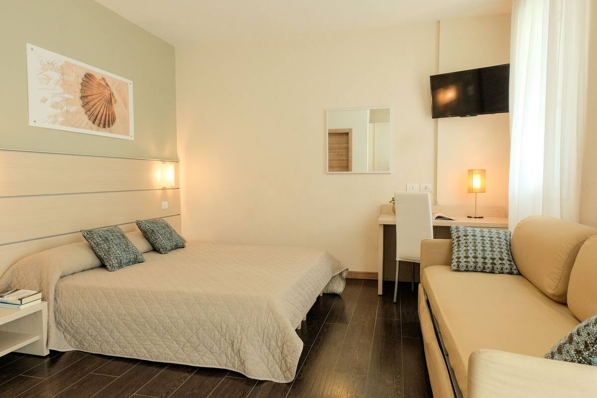 Ein Hotelzimmer mit Bett, Sofa, Schreibtisch, Fernseher und Spiegel.