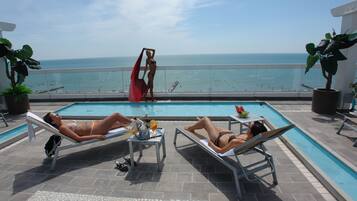 A poolside area with two lounge chairs, a table with drinks, and a view of the ocean.