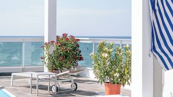 Zona de piscina con vista al mar, una pérgola blanca y plantas en macetas.