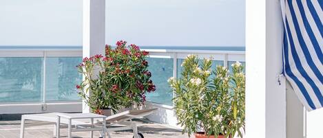 Zona de piscina con vista al mar, una pérgola blanca y plantas en macetas.