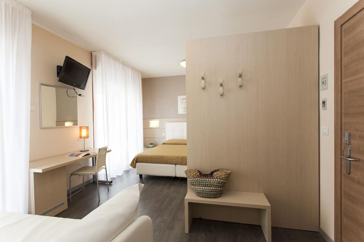 Ein Hotelzimmer mit Bett, Schreibtisch, Stuhl, Fernseher, einem kleinen Tisch und einem Kleiderschrank.