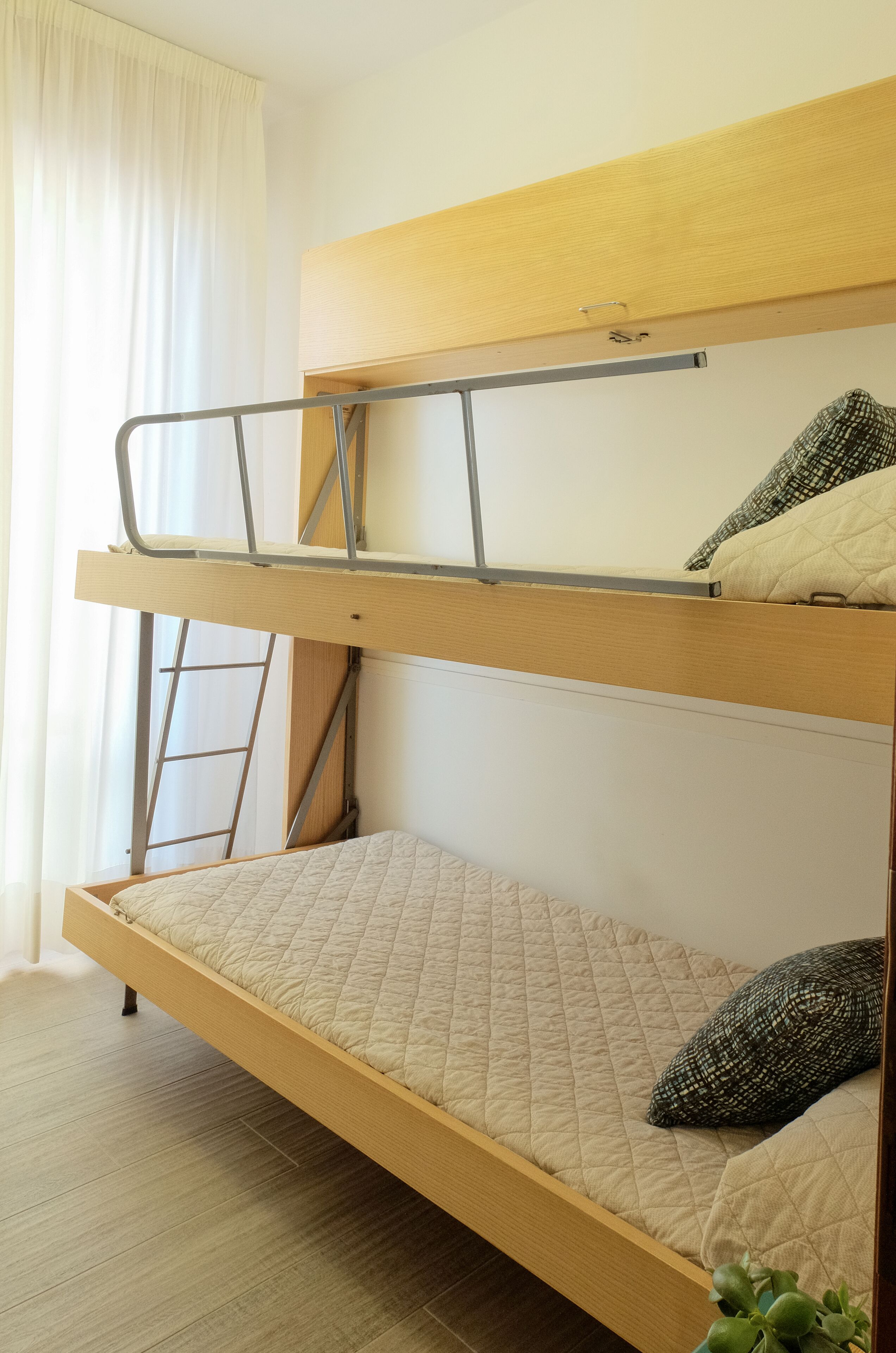 A bunk bed with a ladder, a window with curtains, and a plant on the floor.