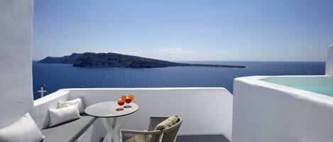 A balcony with a white interior, a round table with a chair, and a view of the sea and a distant island.