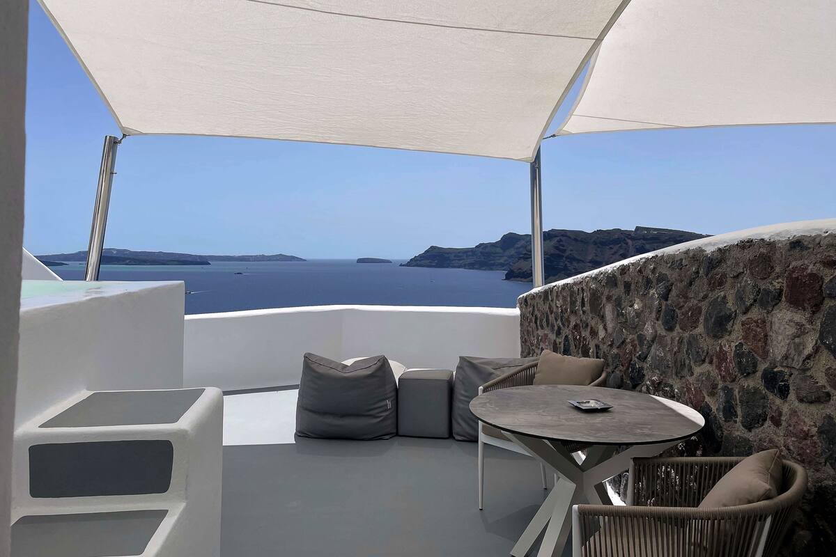 Een terras met uitzicht op zee, stenen muren en buitenmeubilair.