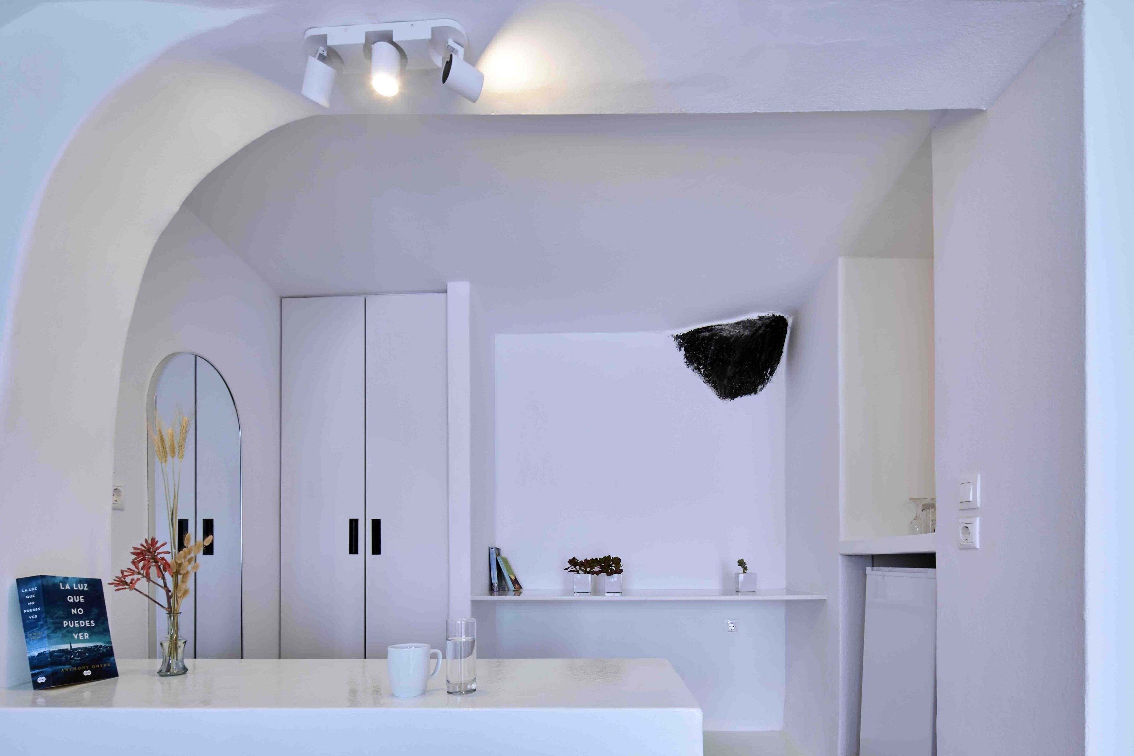 Una habitación de hotel moderna con una decoración en blanco, que presenta un amplio arco de entrada, una recepción blanca, una planta pequeña y un adorno negro en la pared.