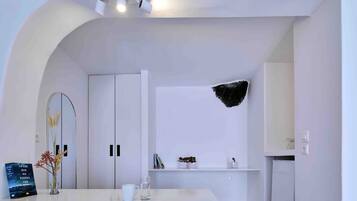 Una habitación de hotel moderna con una decoración en blanco, que presenta un amplio arco de entrada, una recepción blanca, una planta pequeña y un adorno negro en la pared.