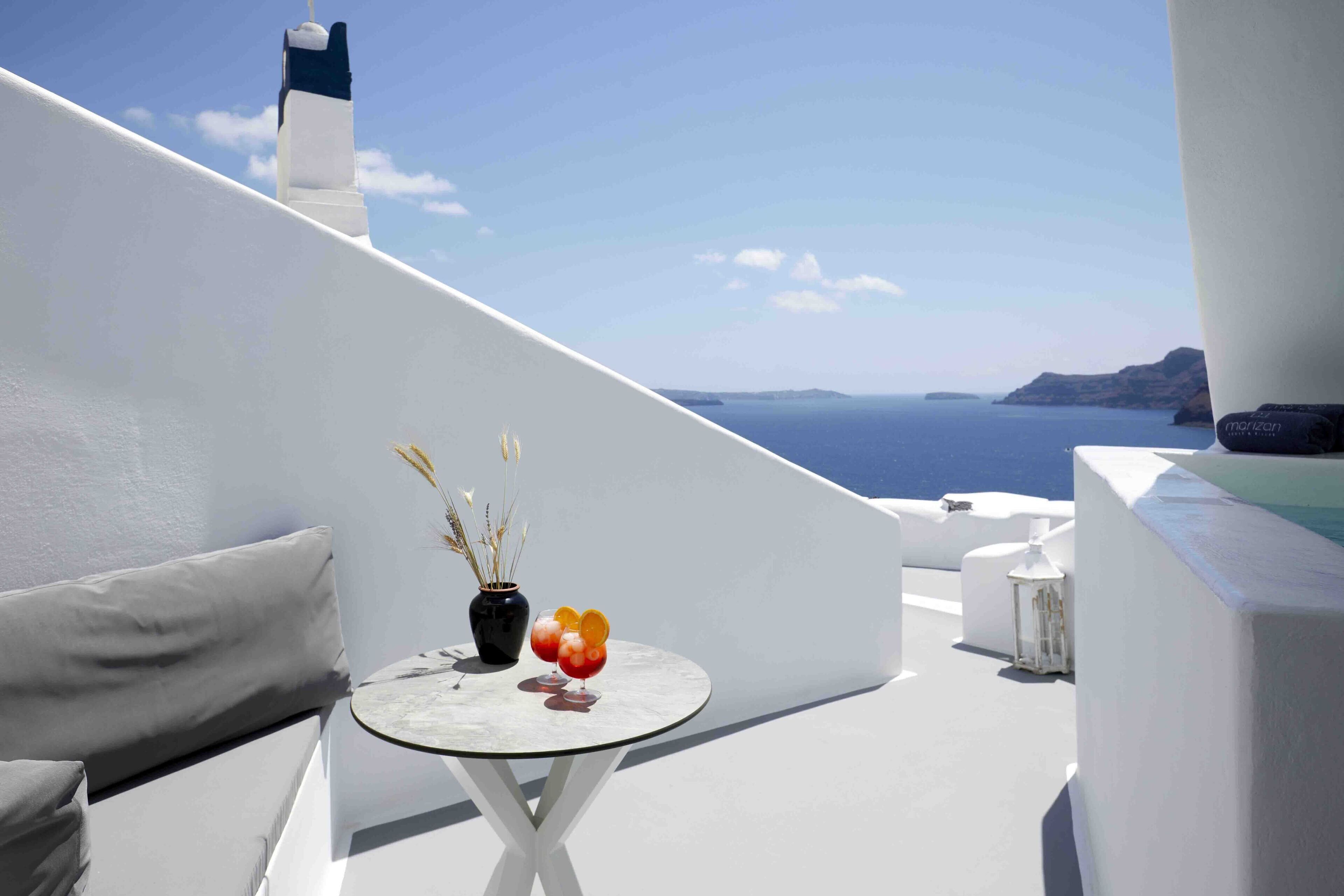A white balcony with a round table, a vase with dried plants, and two drinks.