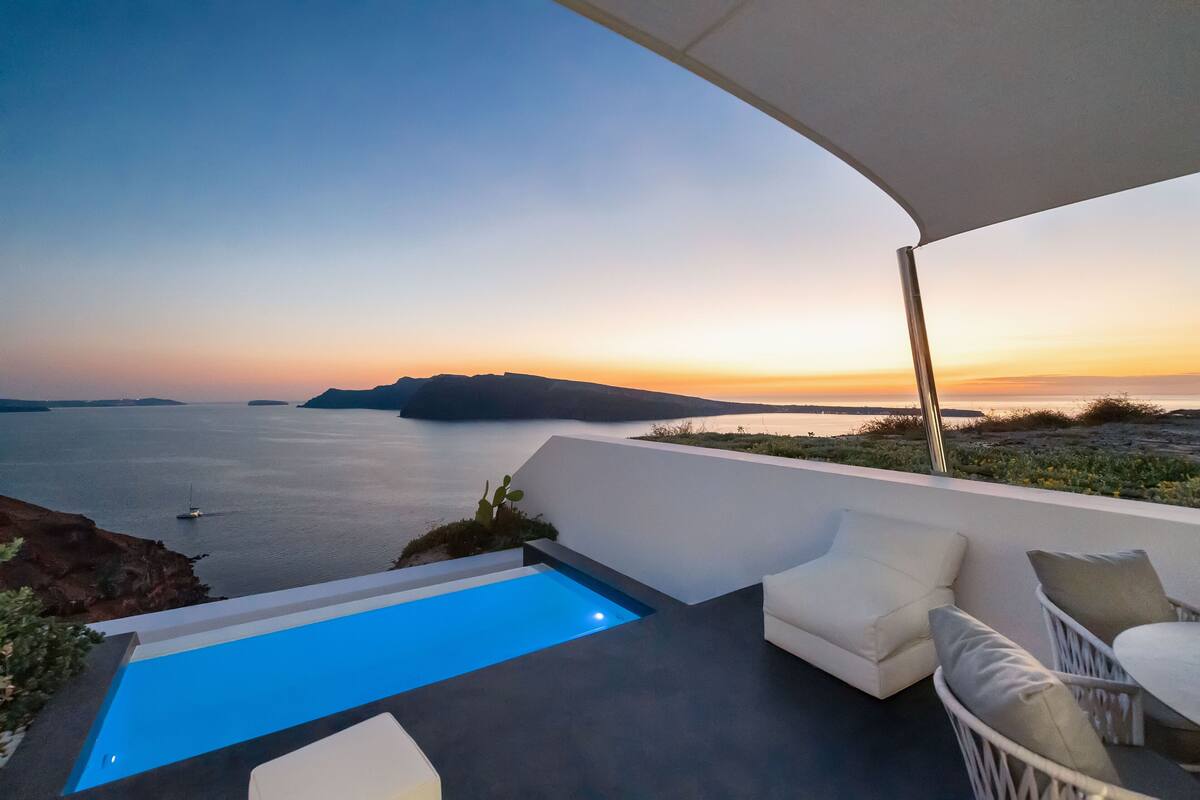 Een modern terras buiten met een zwembad, witte meubels en uitzicht op zee bij zonsondergang.