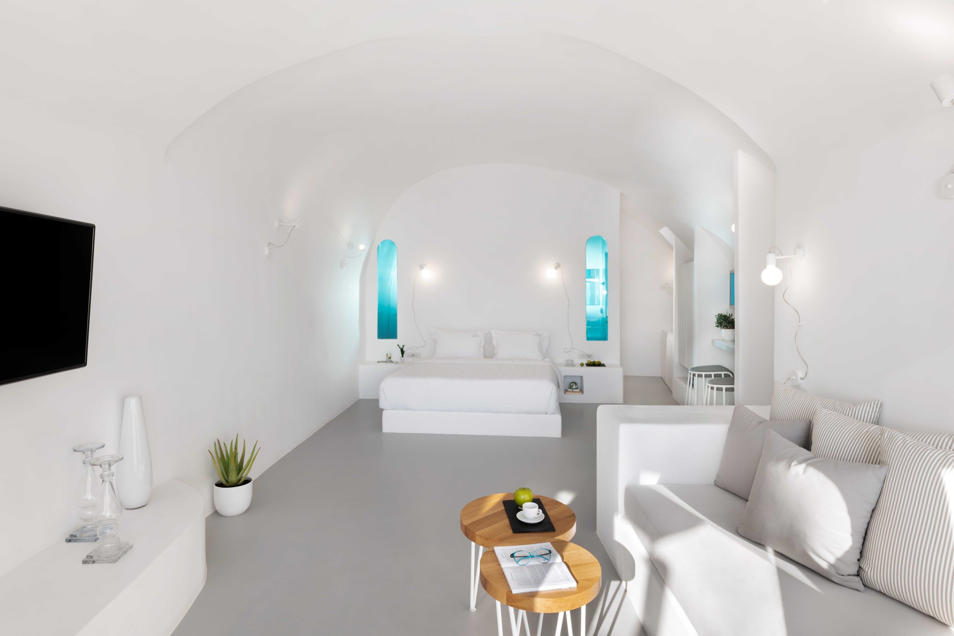 Habitación de hotel moderna y minimalista con una cama grande, una zona de estar con una mesita y un televisor montado en la pared.