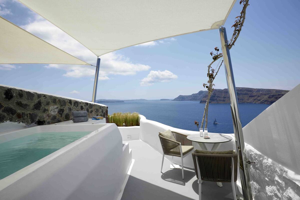 Een balkon met een wit bad, een tafel en stoelen, met uitzicht op water en land in de verte.