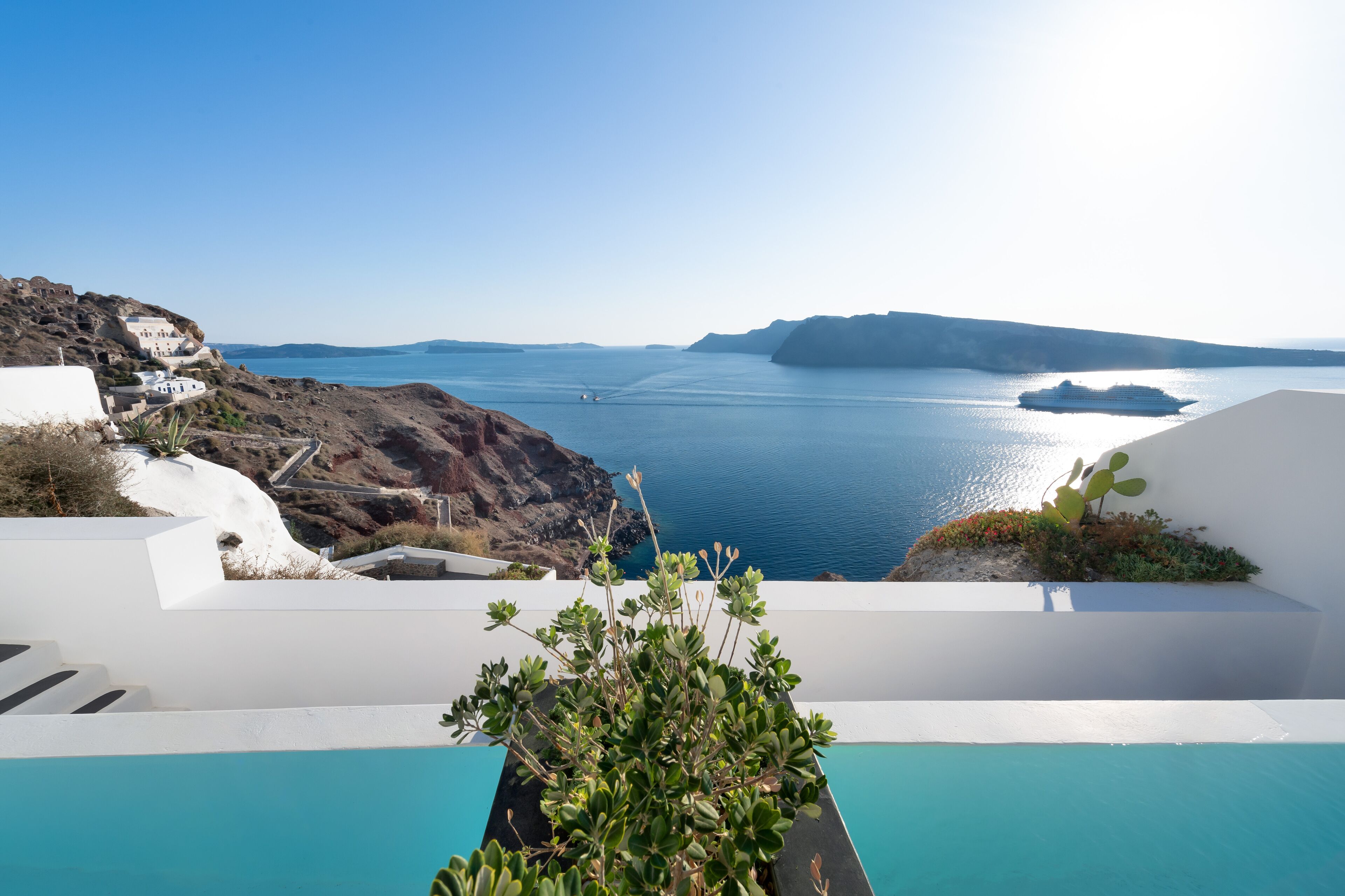 A coastal view with a pool, white buildings, and a clear blue sea.