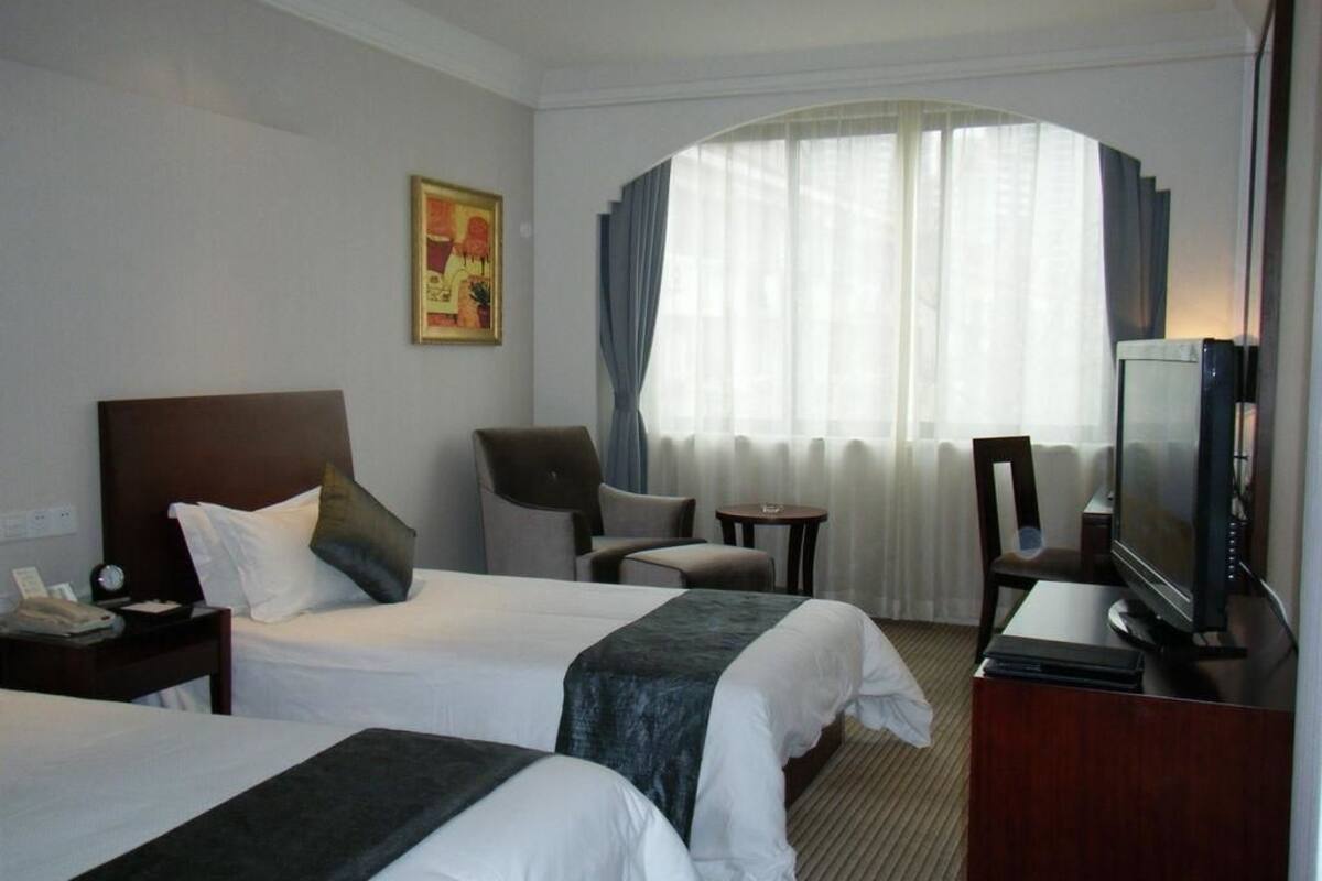 A hotel room with two beds, a TV, a desk, a chair, and a window with curtains.