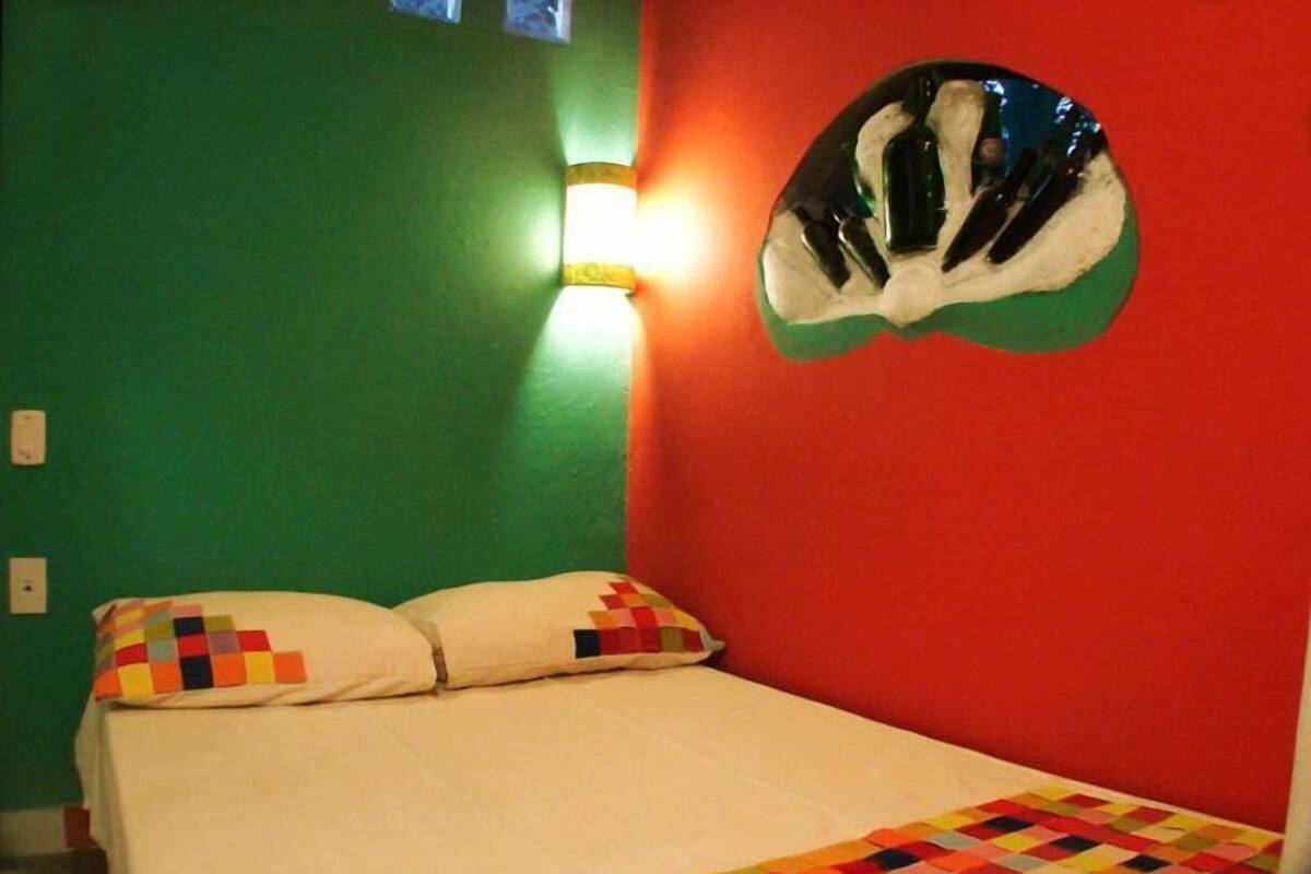 A room with a bed, green walls, a red accent wall, and a unique helmet-shaped mirror.