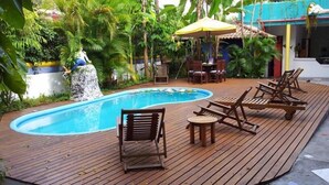 A wooden deck with a pool, lounge chairs, and a table. - Aos Sinos dos Anjos Art Hotel (Arraial d'Ajuda)