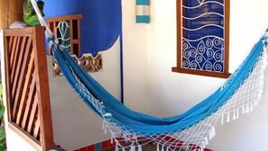 A hammock tied between two wooden posts, a window with decorative patterns, and a small wooden shelf with a plant. - Aos Sinos dos Anjos Art Hotel (Arraial d'Ajuda)