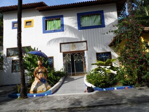 A building with a tiled entrance, a decorative gate, and a statue of a woman holding an umbrella. - Aos Sinos dos Anjos Art Hotel (Arraial d'Ajuda)