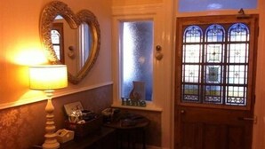 A room with a wooden door, a mirror, a lamp, and a window with stained glass.