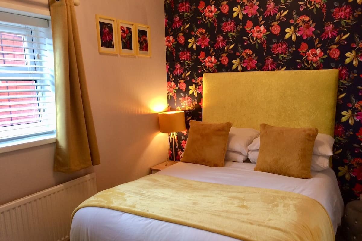 A hotel room with a bed, a nightstand with a lamp, and a window with blinds.