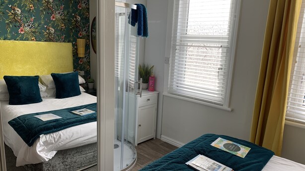 A hotel room with two beds, a shower, a window with blinds, and a floral wallpaper.
