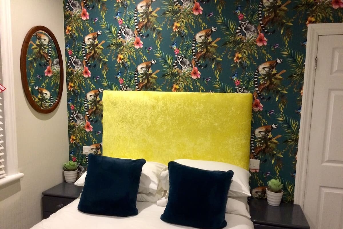 A bed with two pillows, a yellow headboard, and a floral wallpaper.