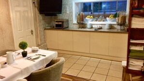 A dining area with a table set for two, a television mounted above the counter, and a window with a view of the outside.