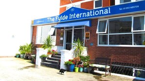 The Fylde International hotel with a blue awning, brick facade, and outdoor seating area with potted plants.