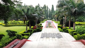 A pathway leading through a well-maintained garden with neatly trimmed hedges and palm trees. - Ambassador Ajanta (Chhatrapati Sambhajinagar)