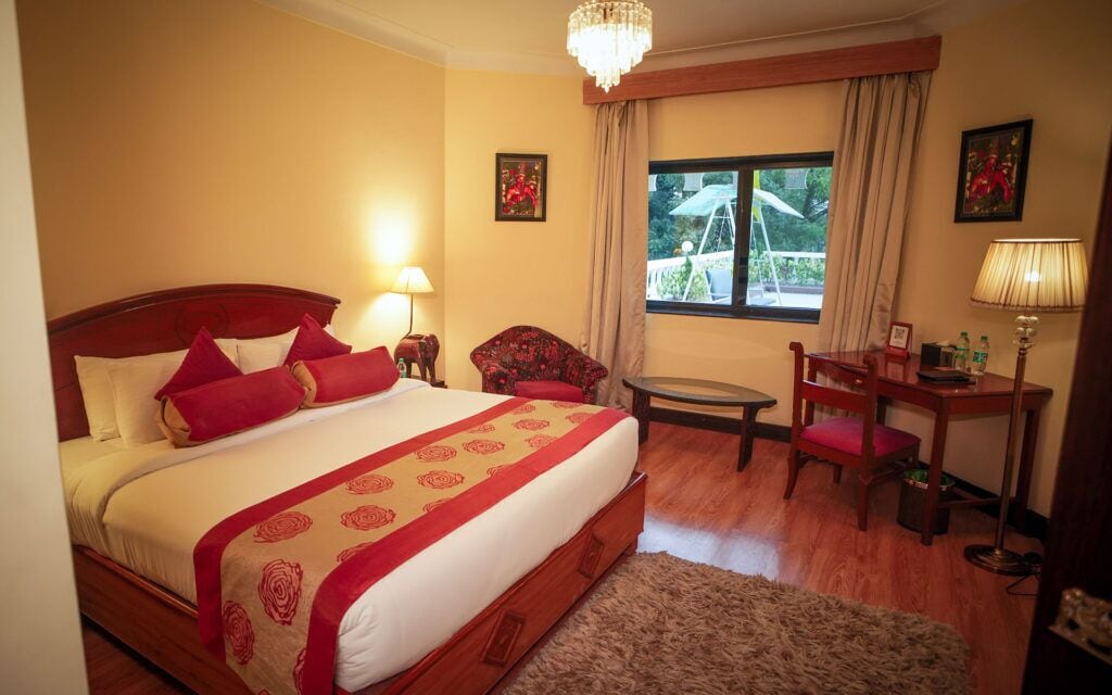 A hotel room with a large bed, a desk, a chair, a small table, and a window with curtains.