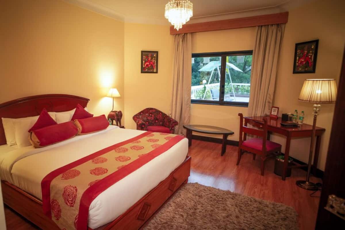 Habitación de hotel con una cama grande, un escritorio, una silla, una mesita y una ventana con cortinas.