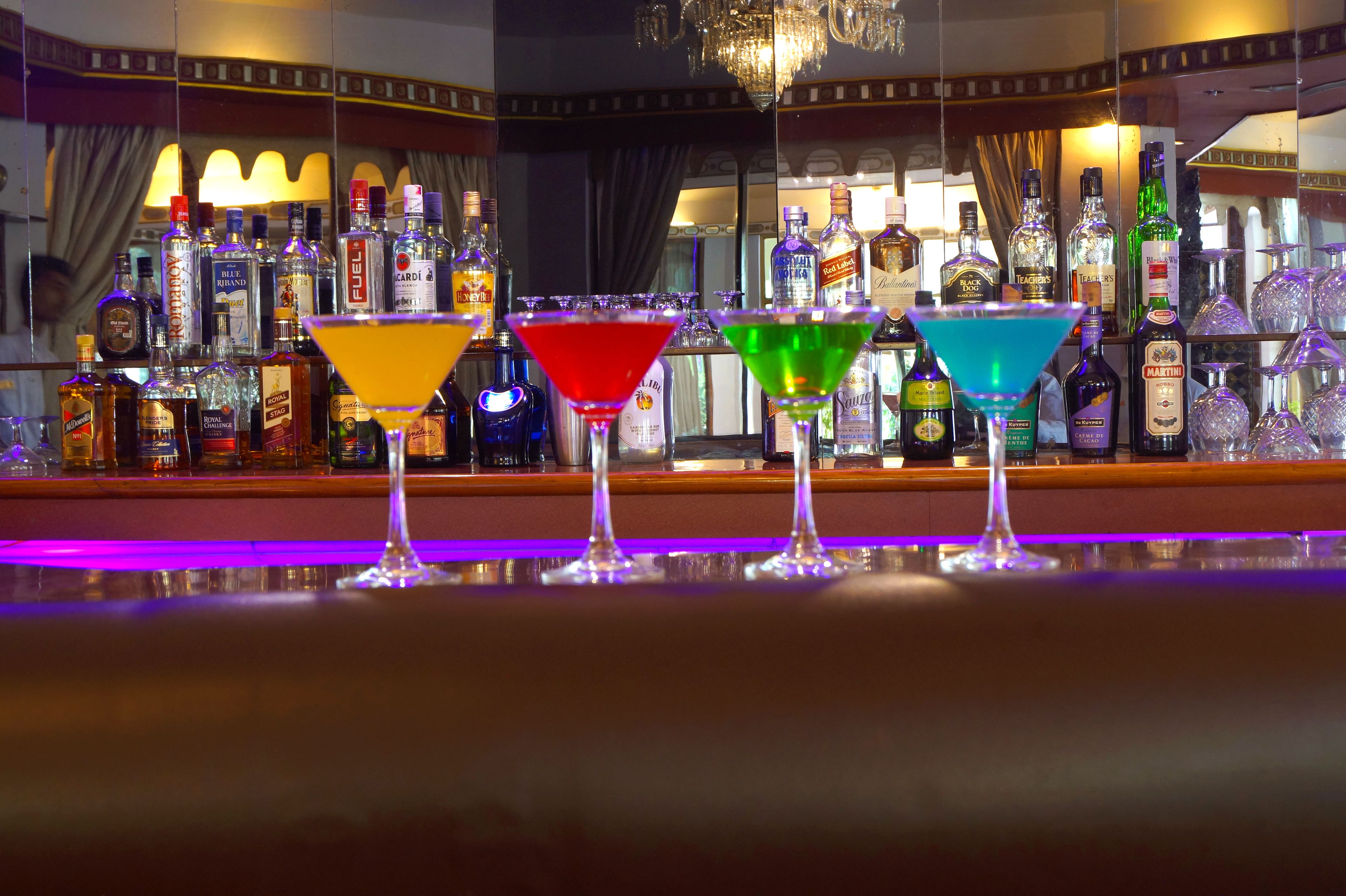 Un bar con una variedad de botellas de licor y tres coloridos vasos de martini.