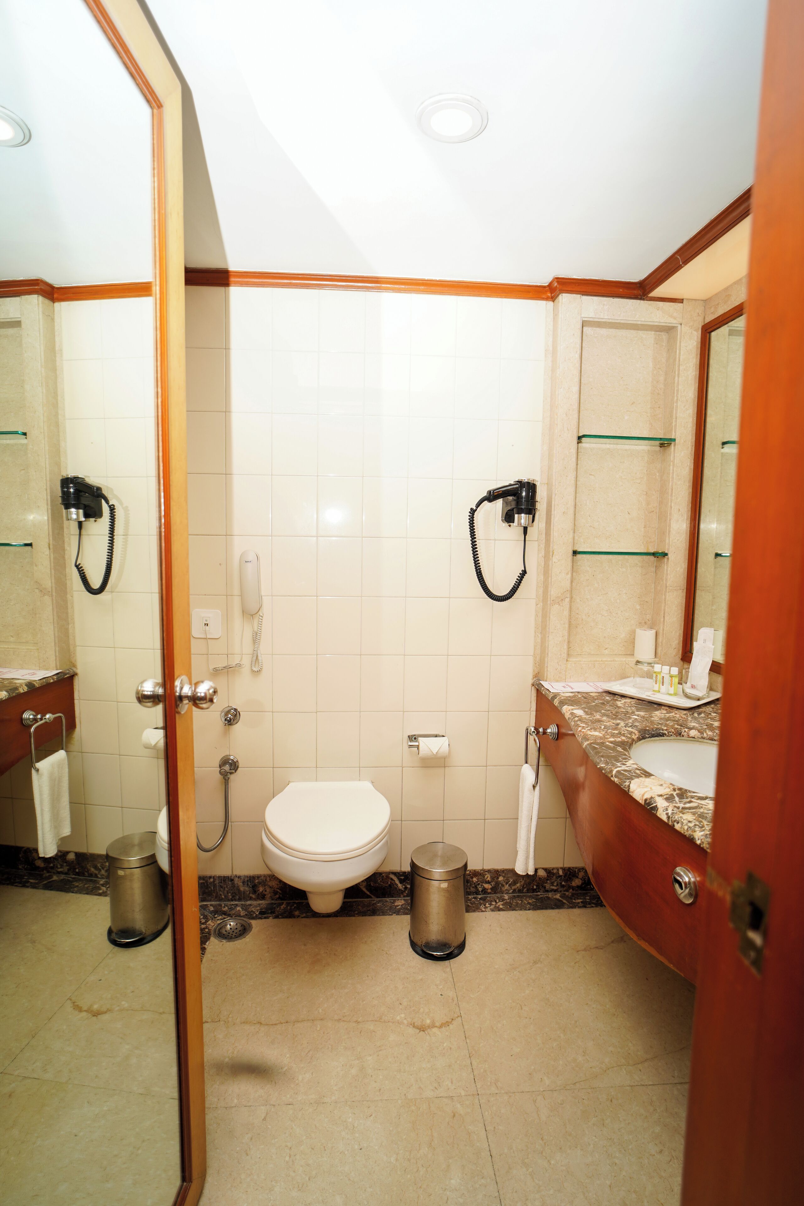 Une salle de bain équipée de toilettes, d’un lavabo et de miroirs. On y trouve également des sèche-cheveux et un téléphone fixé au mur.