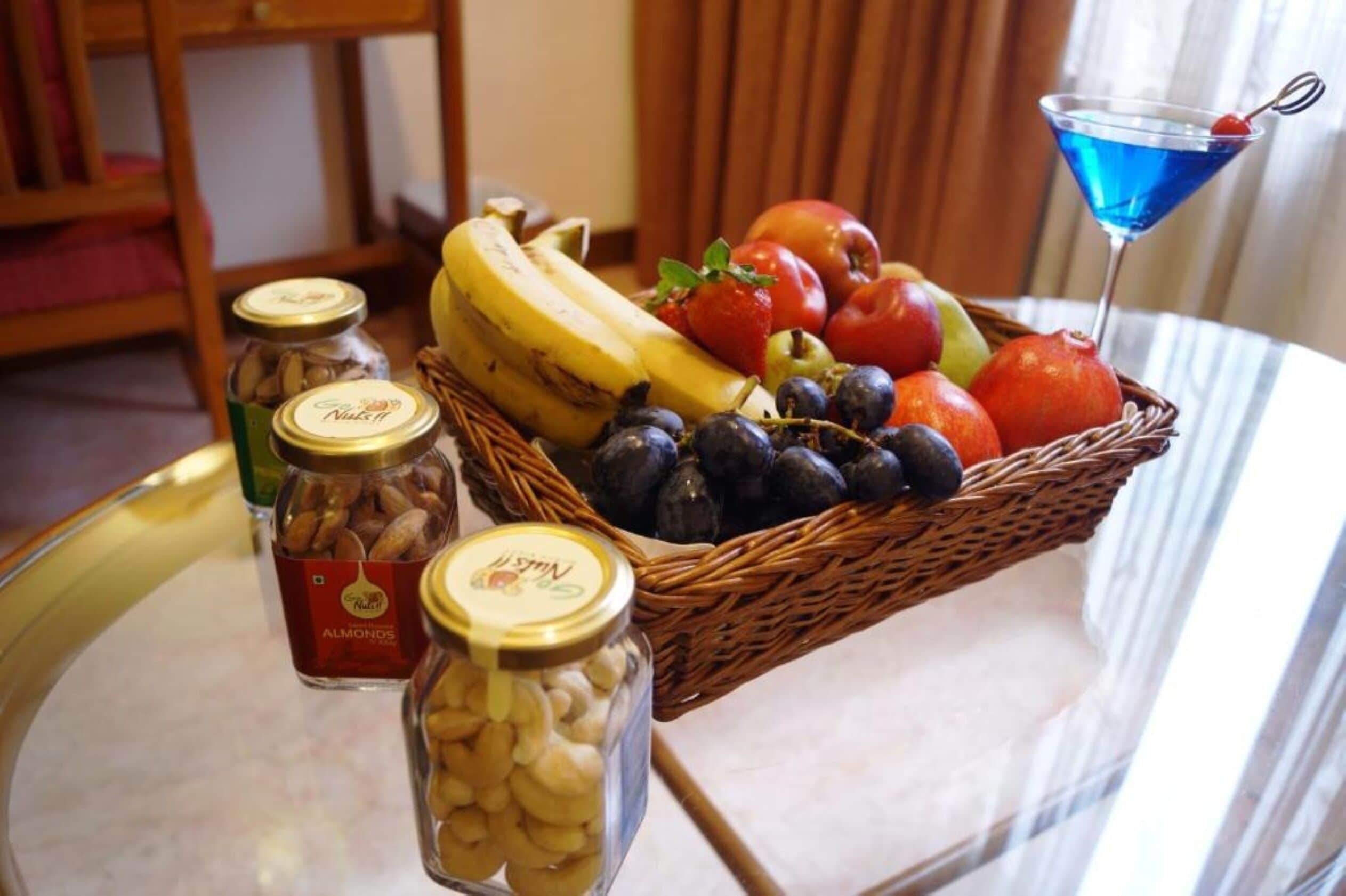 A table with a fruit basket, jars of nuts, and a martini glass.