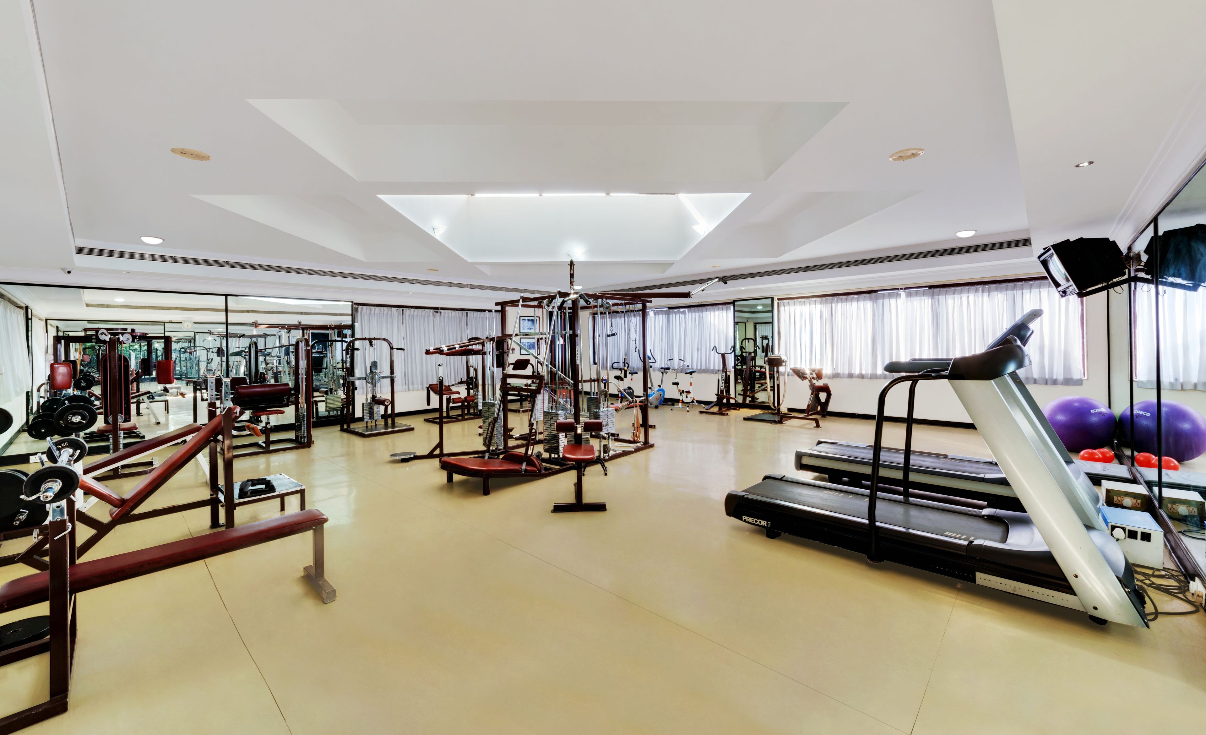 Un gimnasio amplio con diversos equipos de ejercicio, incluyendo cintas de correr, máquinas de pesas y pesas sueltas.