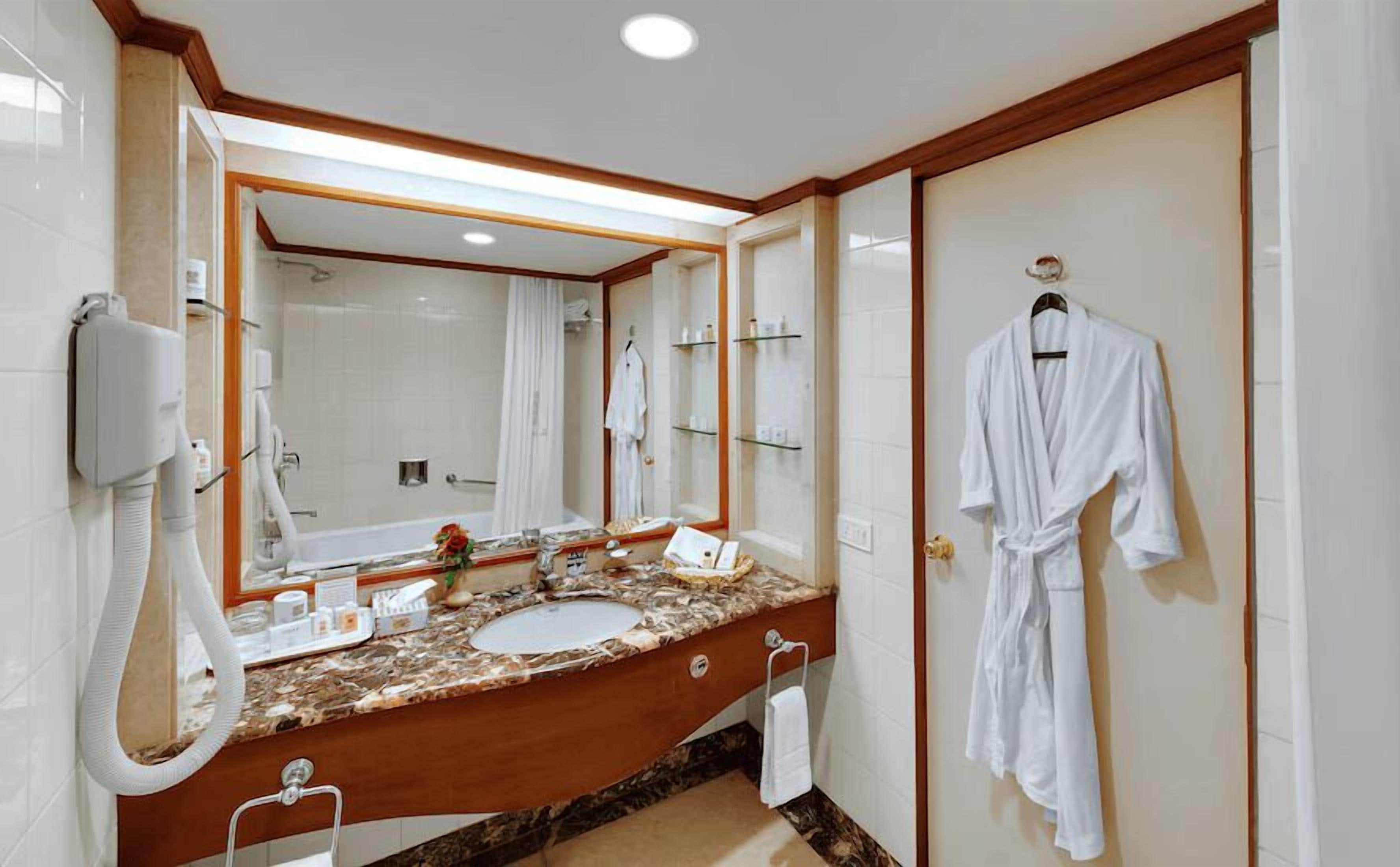 Ein Badezimmer mit einem großen Spiegel, einem Waschbecken, einem an der Wand hängenden Bademantel und einem Handtuchhalter.