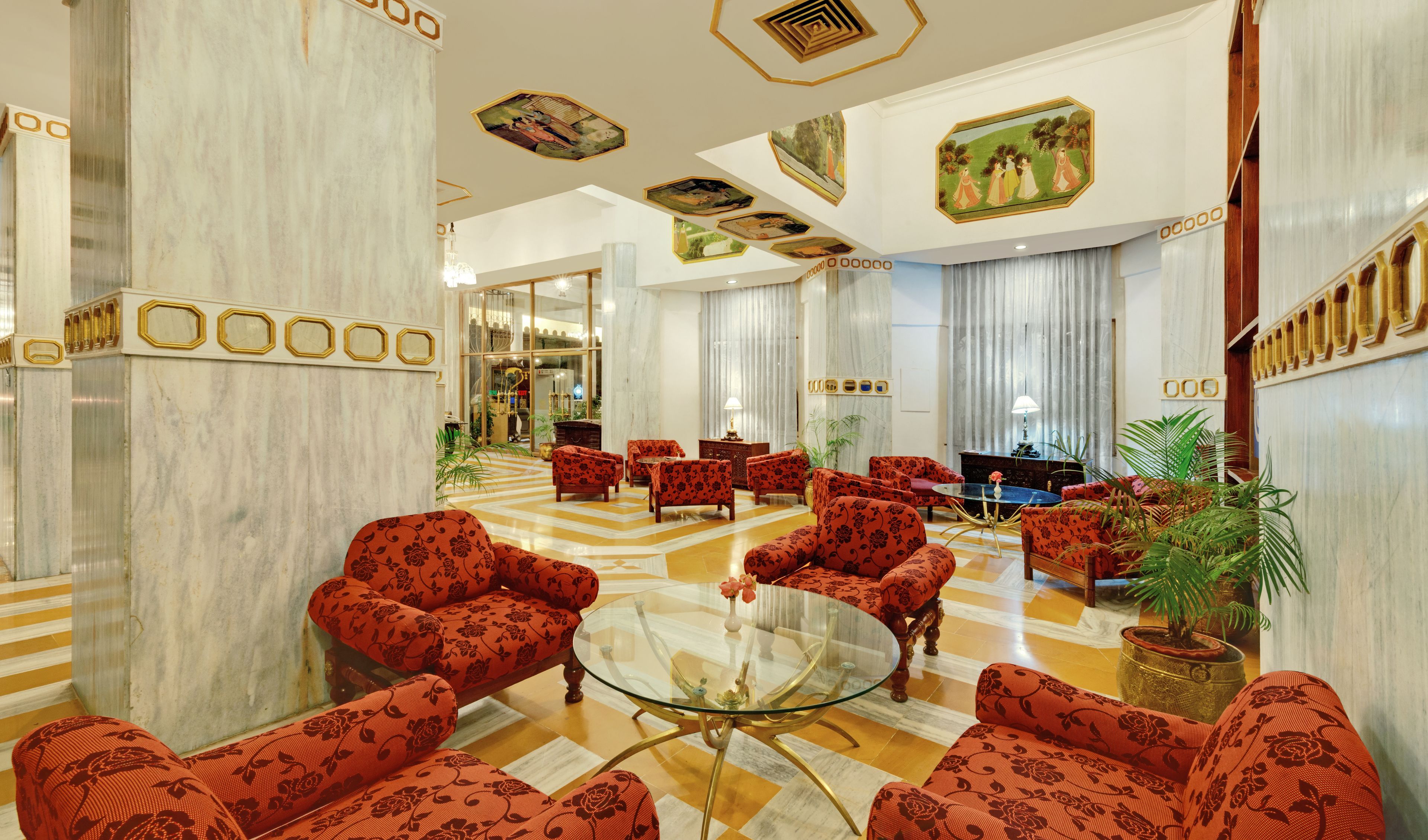A spacious lobby with a marble floor, red patterned sofas, a glass coffee table, and a large mirror.
