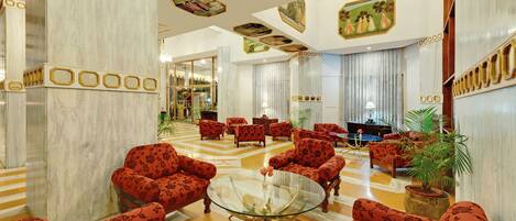 A spacious lobby with a marble floor, red patterned sofas, a glass coffee table, and a large mirror.