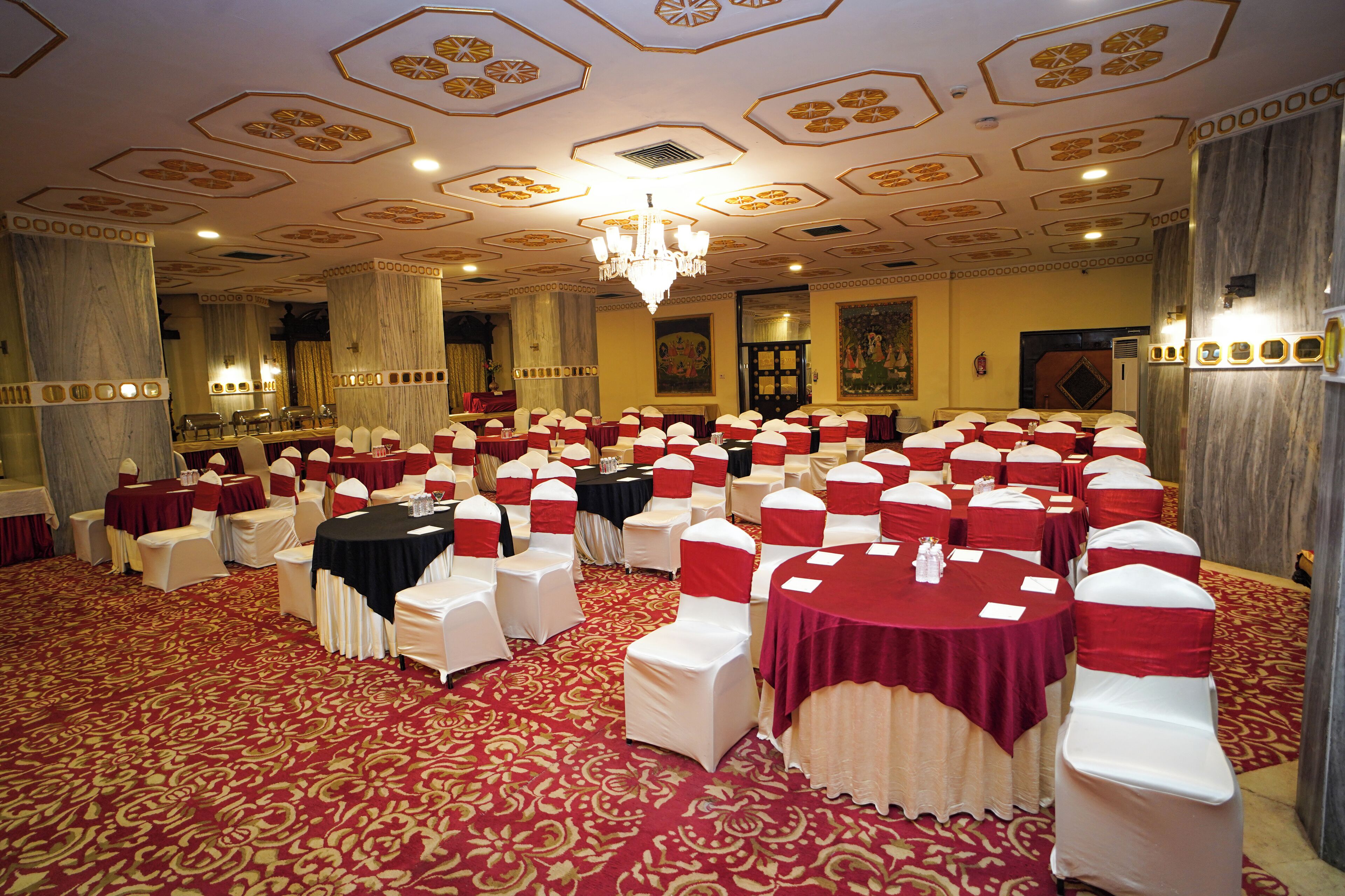 A banquet hall with round tables and chairs, a chandelier, and a patterned carpet.