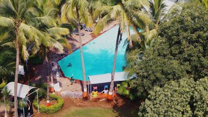 An aerial view of a resort with a swimming pool surrounded by palm trees and a beach area with lounge chairs. - Ambassador Ajanta (Chhatrapati Sambhajinagar)