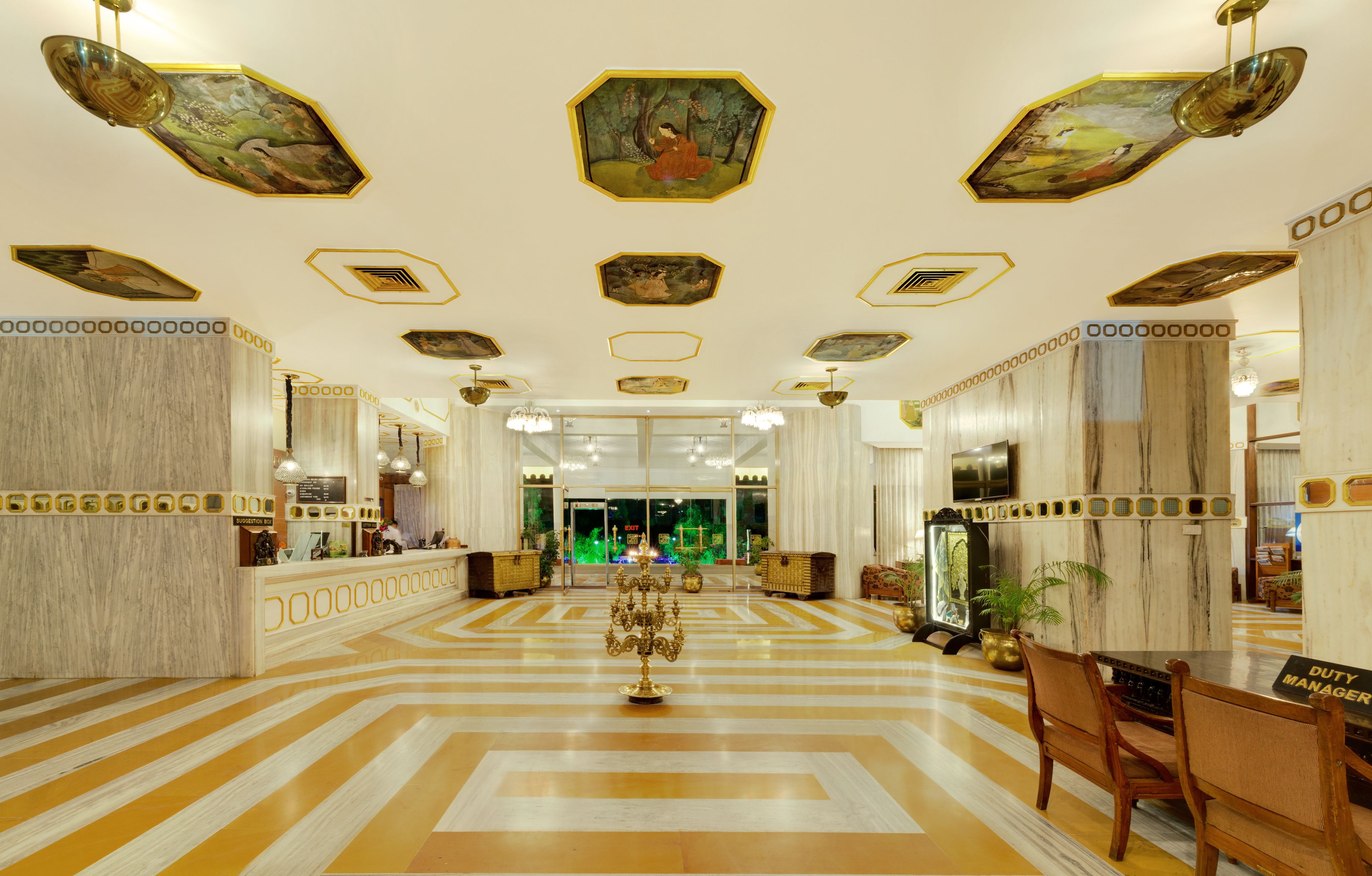A hotel lobby with a check-in counter, a reception desk, a chandelier, and a decorative candelabra.