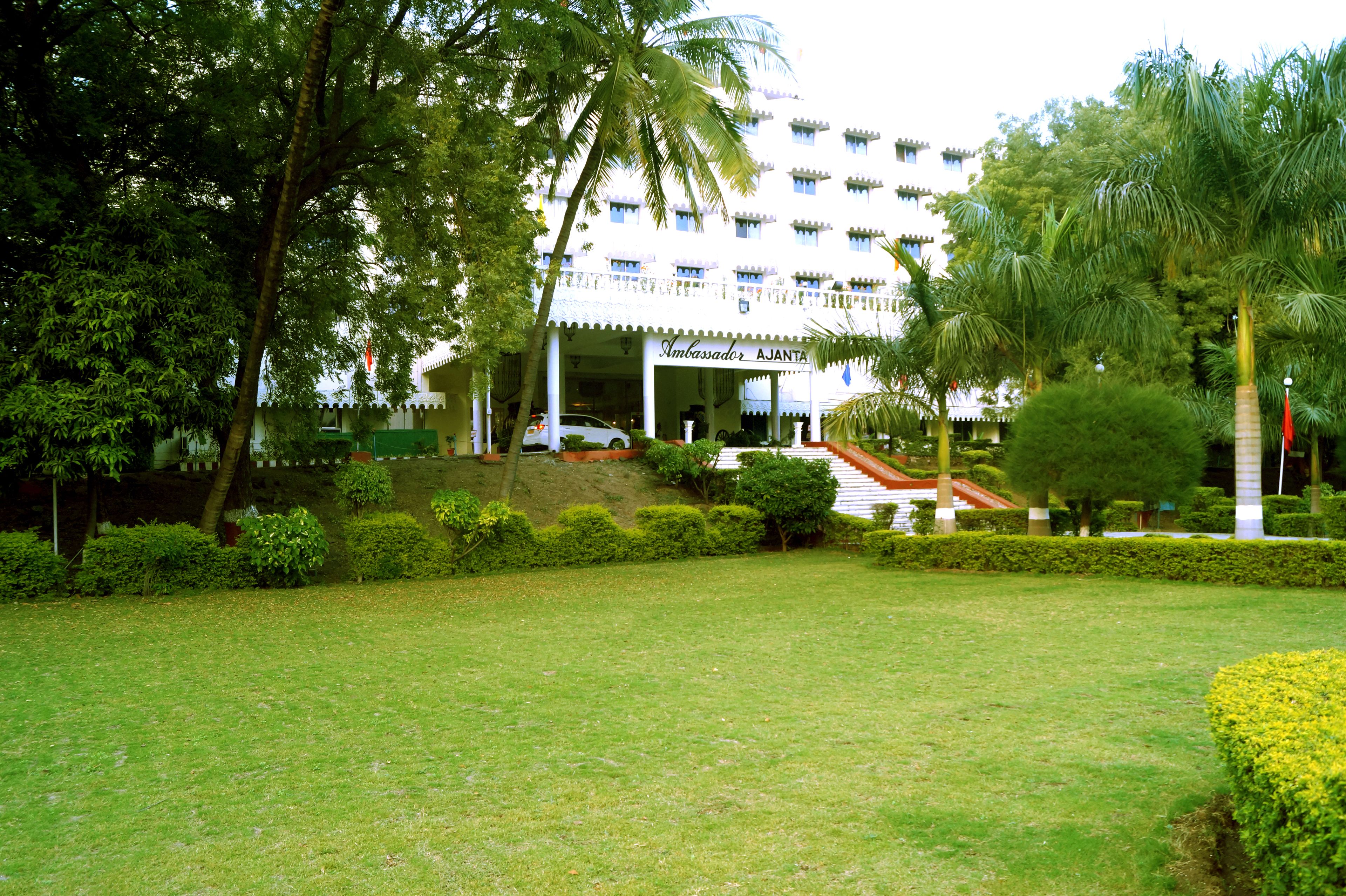 Un hotel de fachada blanca, palmeras y un césped cuidado.