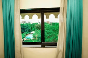 Una ventana con vista a una piscina rodeada de vegetación y un edificio con arcos al fondo.