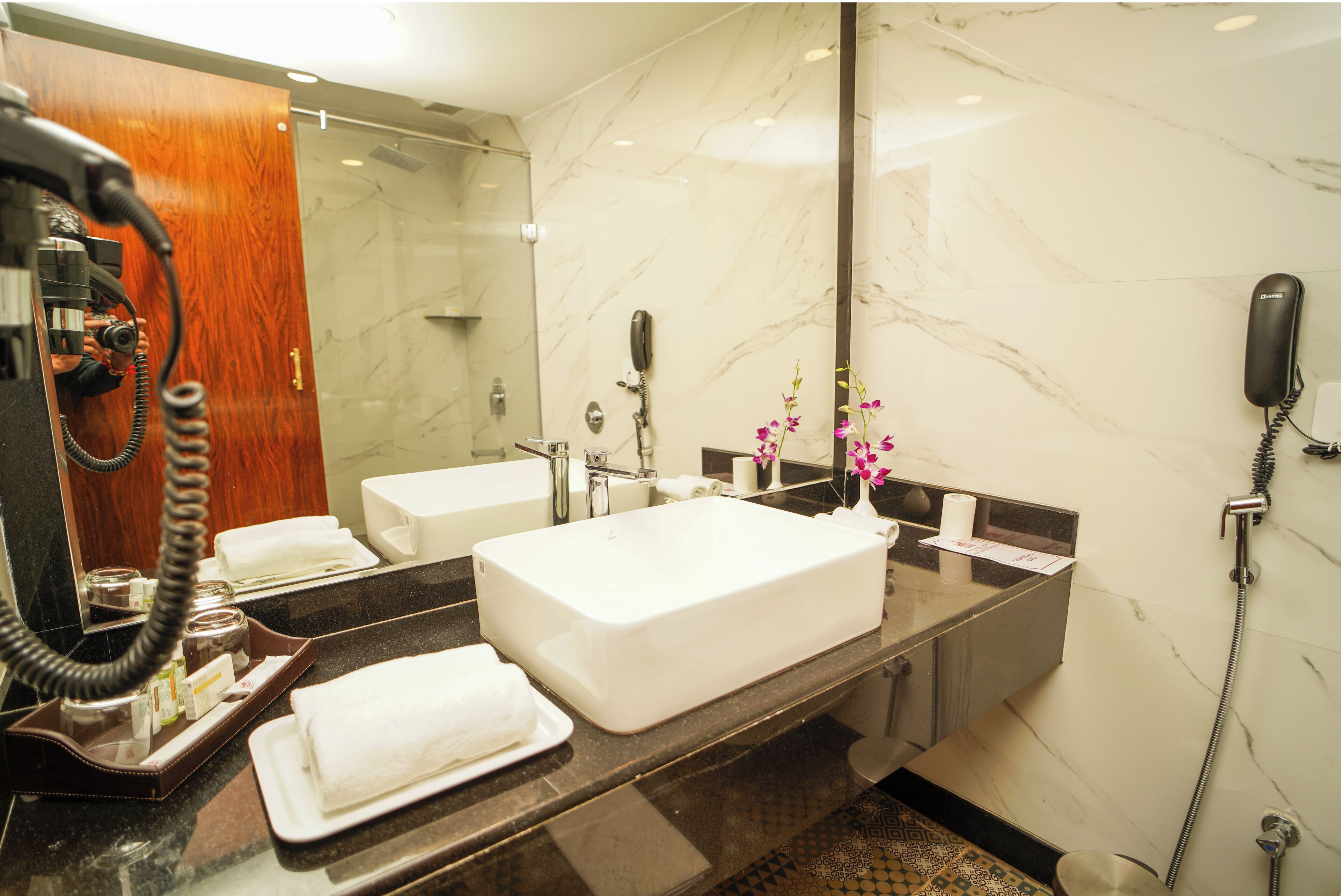 Un baño de hotel con un espejo grande, un lavamanos blanco, una ducha y un teléfono.