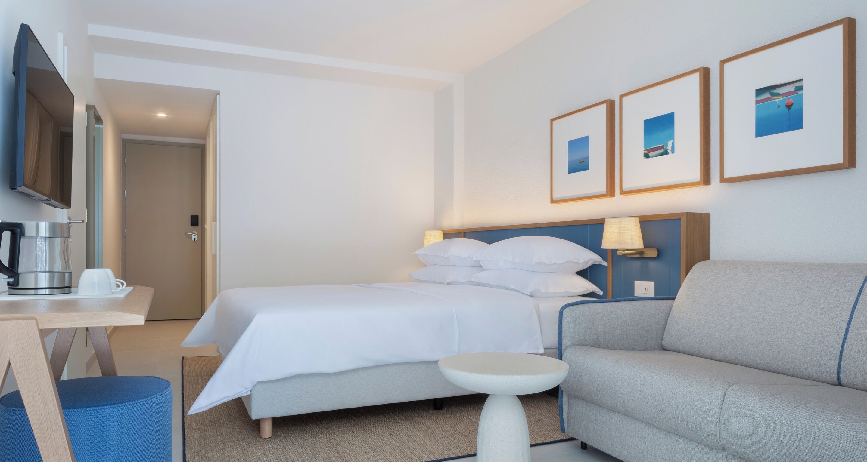 A hotel room with a bed, a sofa, a small table, a coffee maker, and a TV.